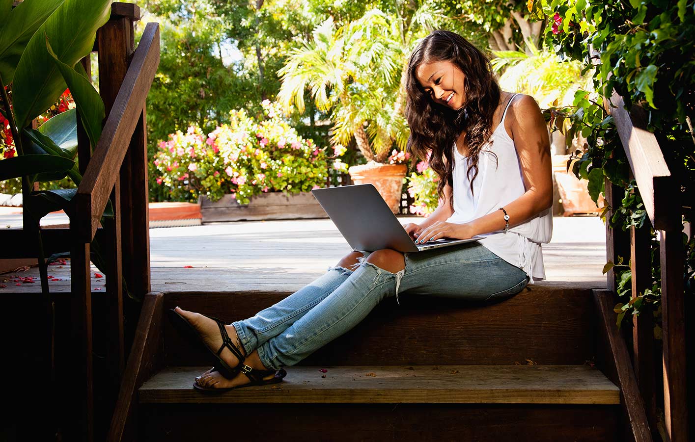 Frau sitzt auf einer Treppe zu einer Terrasse und hat einen Laptop auf dem Schoß